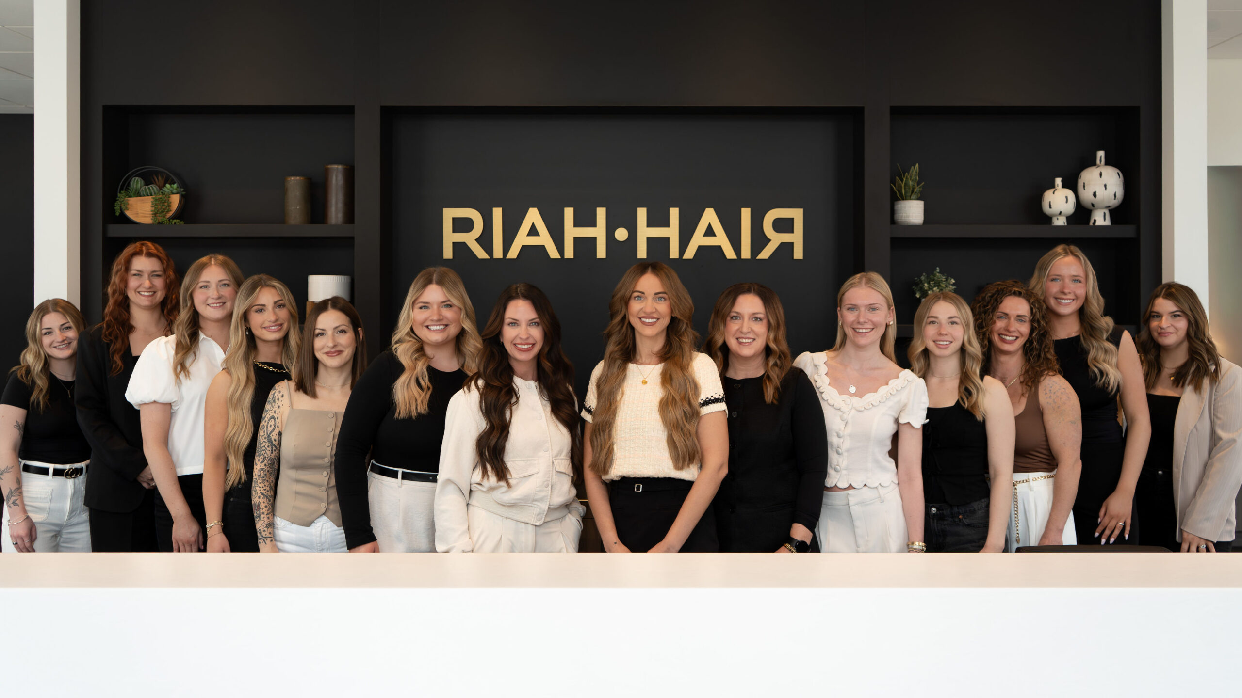 The RIAH•HAIR team in front of the salon logo wall